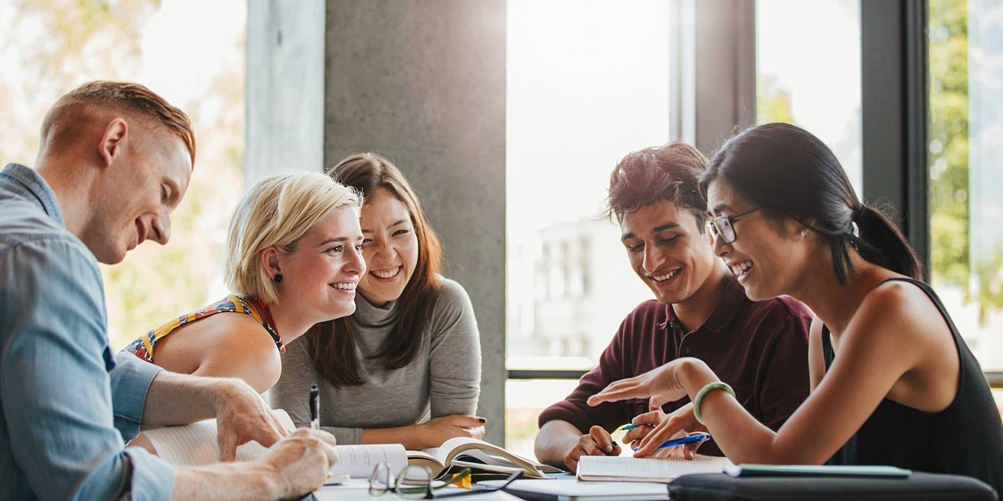 Happy young university students of mixed races studying with books in library. 