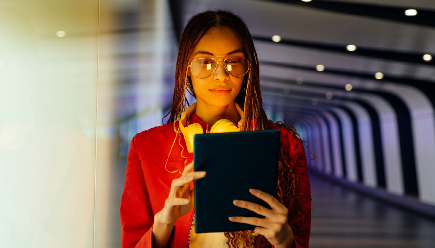 Woman standing in a long hallway with headphones around her neck on a tablet
