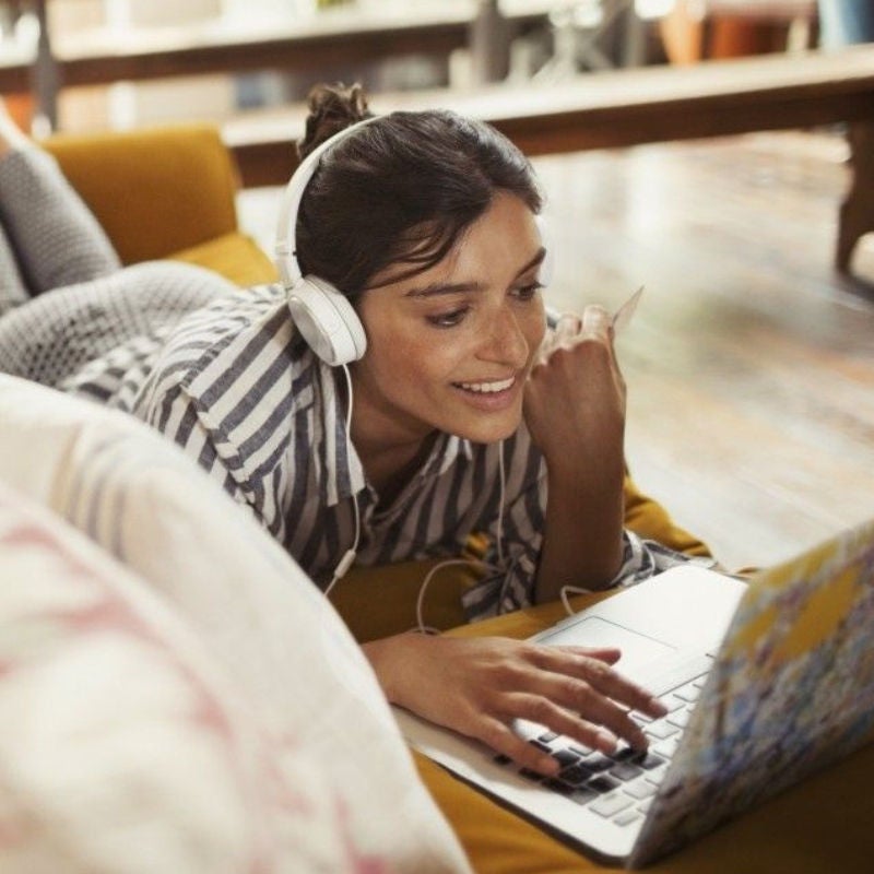 Smiling woman with headphones using laptop on sofa to shop with credit card in hand