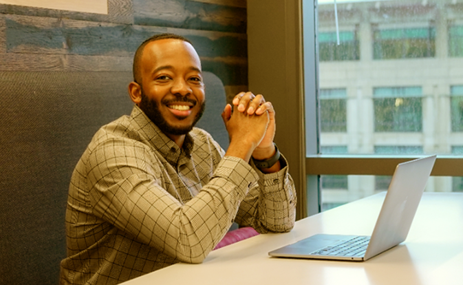 Smiling man working on a laptop in a modern office, looking happy and confident.