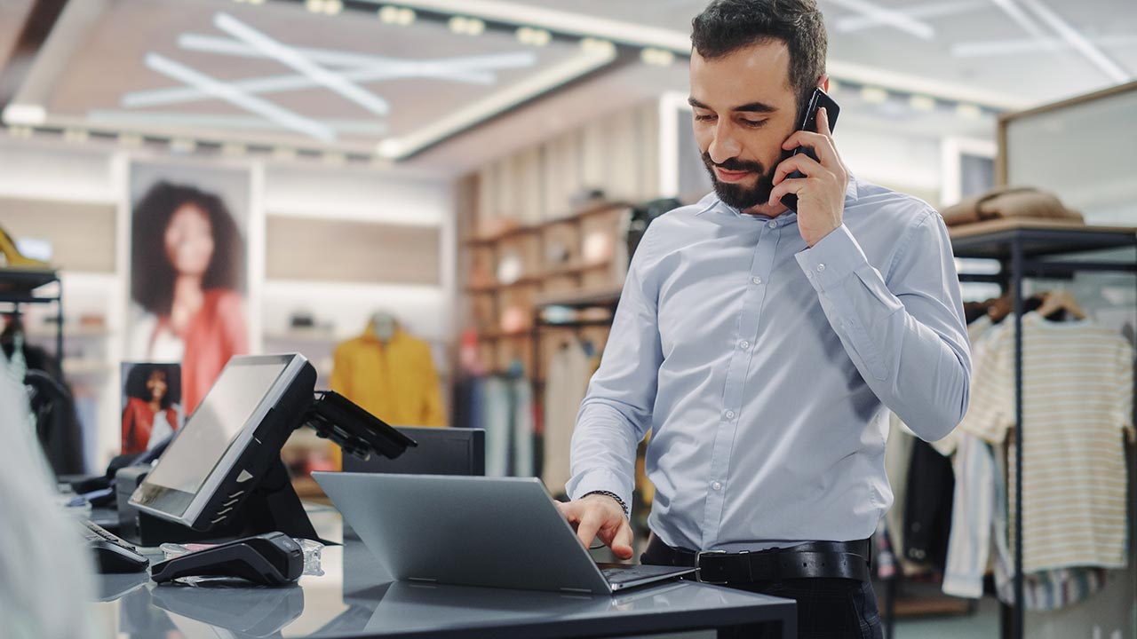 Male retail owner using phone and laptop.