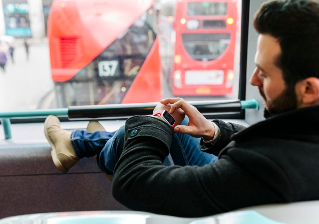 UK, London, young man in a double-decker bus using his smartwatch