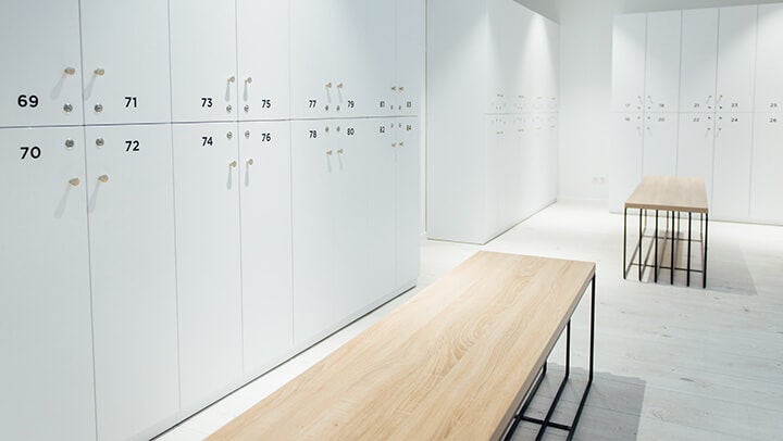 Öltözőszekrények számozott ajtókkal, fa ülőpadokkal világos beltéri térben