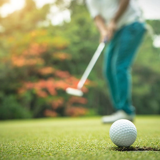 Close up of person hitting golf ball on a course.