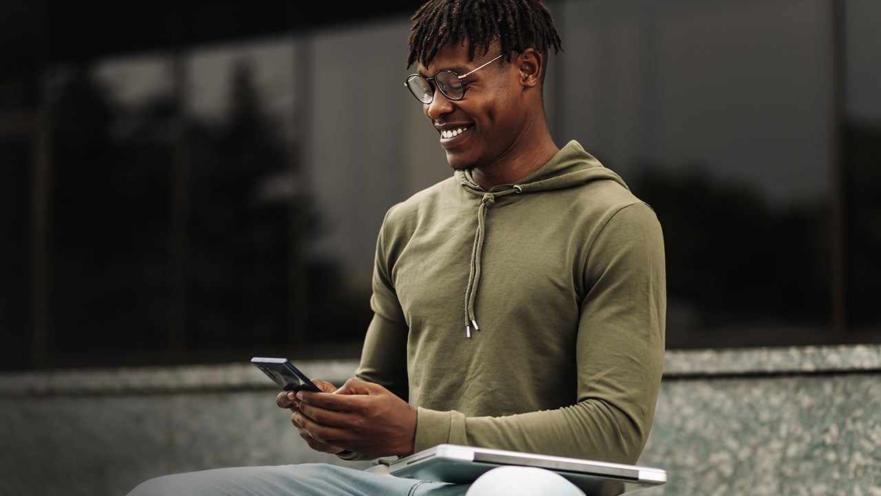 Man using mobile phone, holding laptop outdoors.