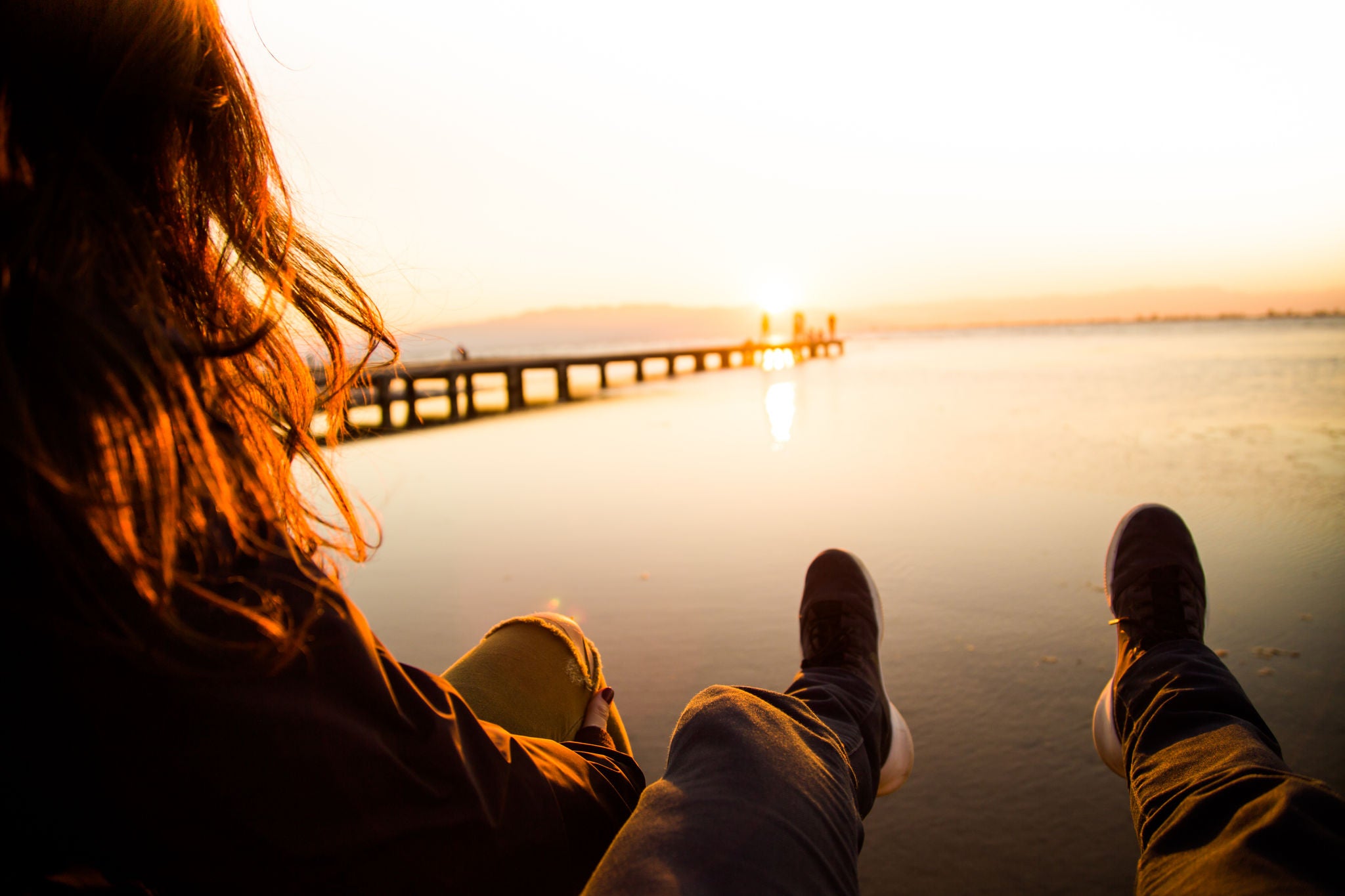 A woman is seen touching her hand while basking in sunlight. The scene captures the beauty of nature with a clear sky, clouds, and a serene beach setting during sunset.