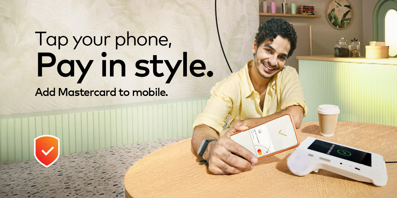 Indian man seated at a booth tapping phone on payment machine to pay with his Mastercard card