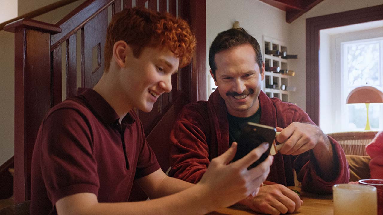 Två personer sitter vid ett bord och tittar på en mobiltelefon.