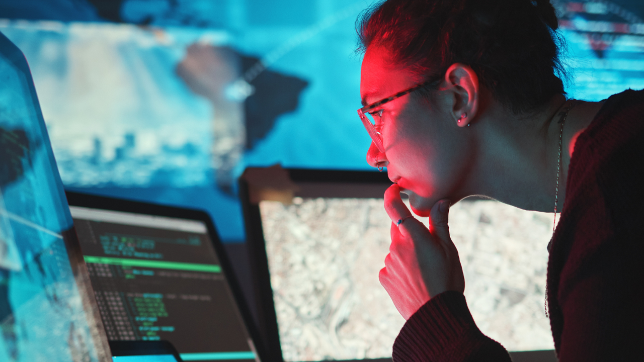 a woman looks at at a computer screen in front of a screen showing a map of South America