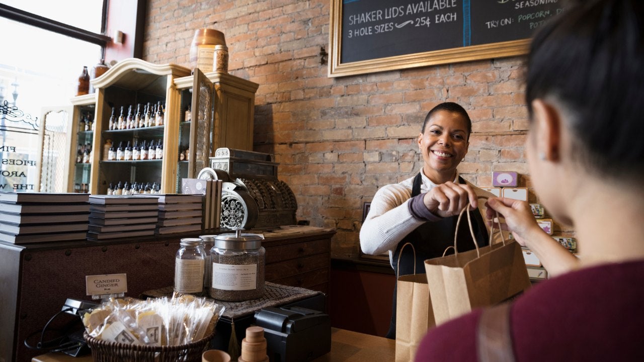 A woman shopkeeper hands a bag to a customer. 