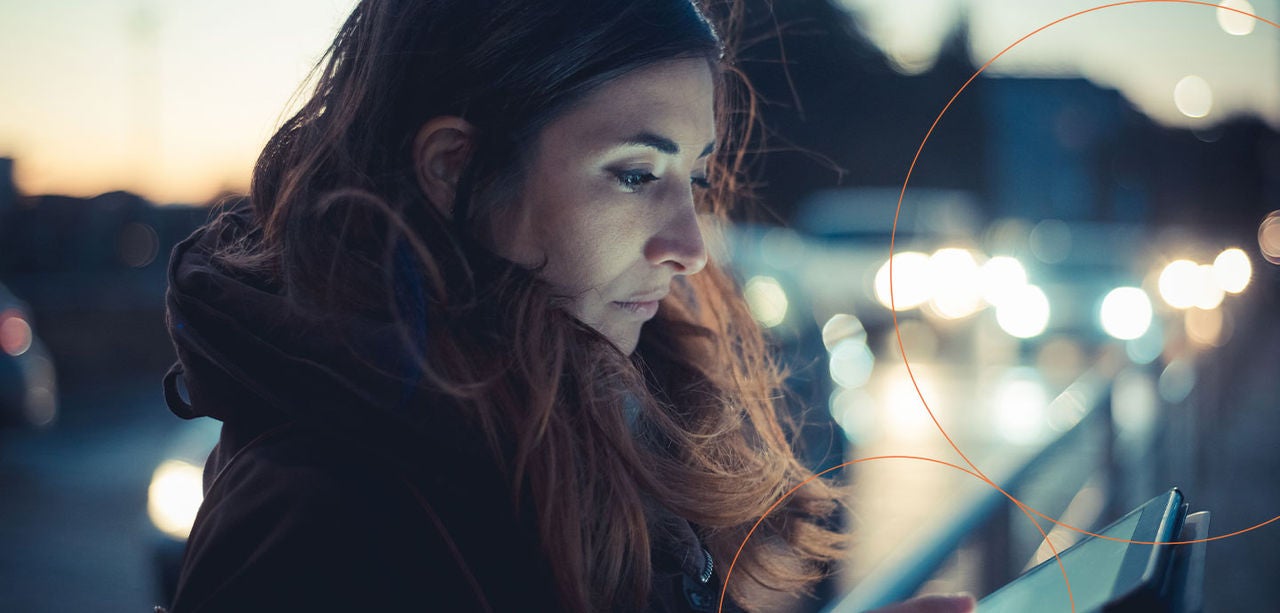 Et nærbillede-portræt af en kvinde, der bruger en tablet udendørs om aftenen.