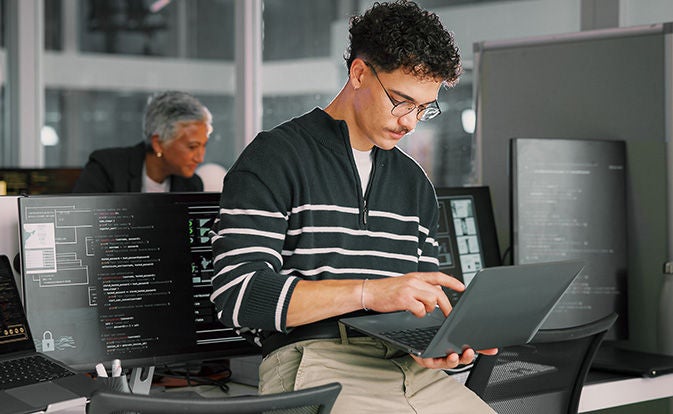 Man working on a laptop while sitting on a desk