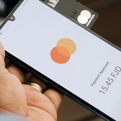 Holding phone with Mastercard new payment acceptance solution and Mastercard card behind it.