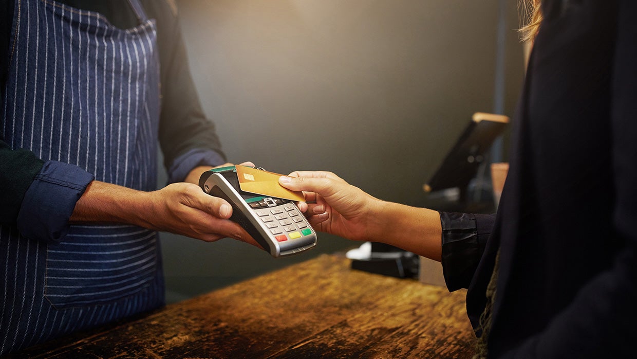 A person taps their card on a payment terminal, indicating a transaction in progress.