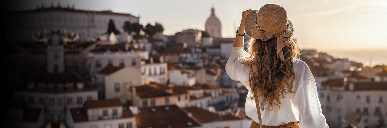 Fiatal nő kalapban városi panorámát fotóz naplementében, utazási és városnéző hangulatban