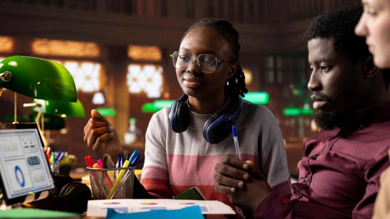 College students in a library look at a computer showing infographics. 