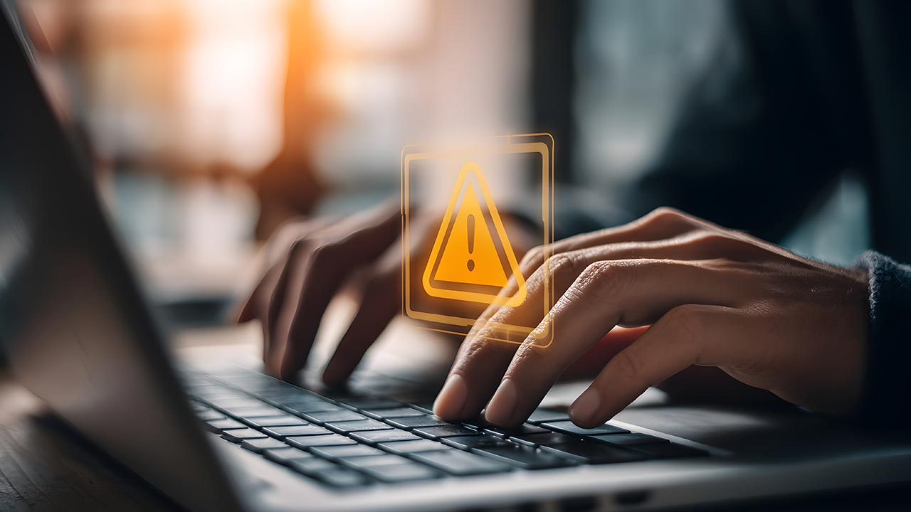 Close up of  hands typing on a laptop with security alert overlay.