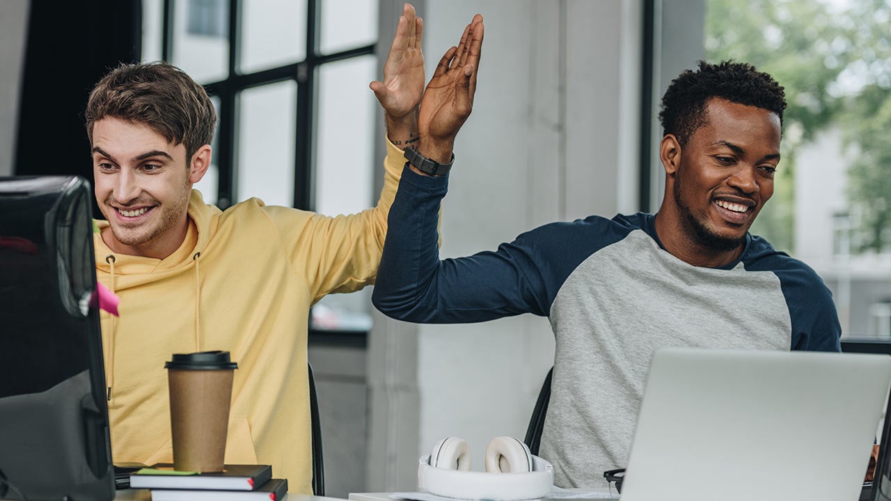 Programmers giving high five while working in office together.