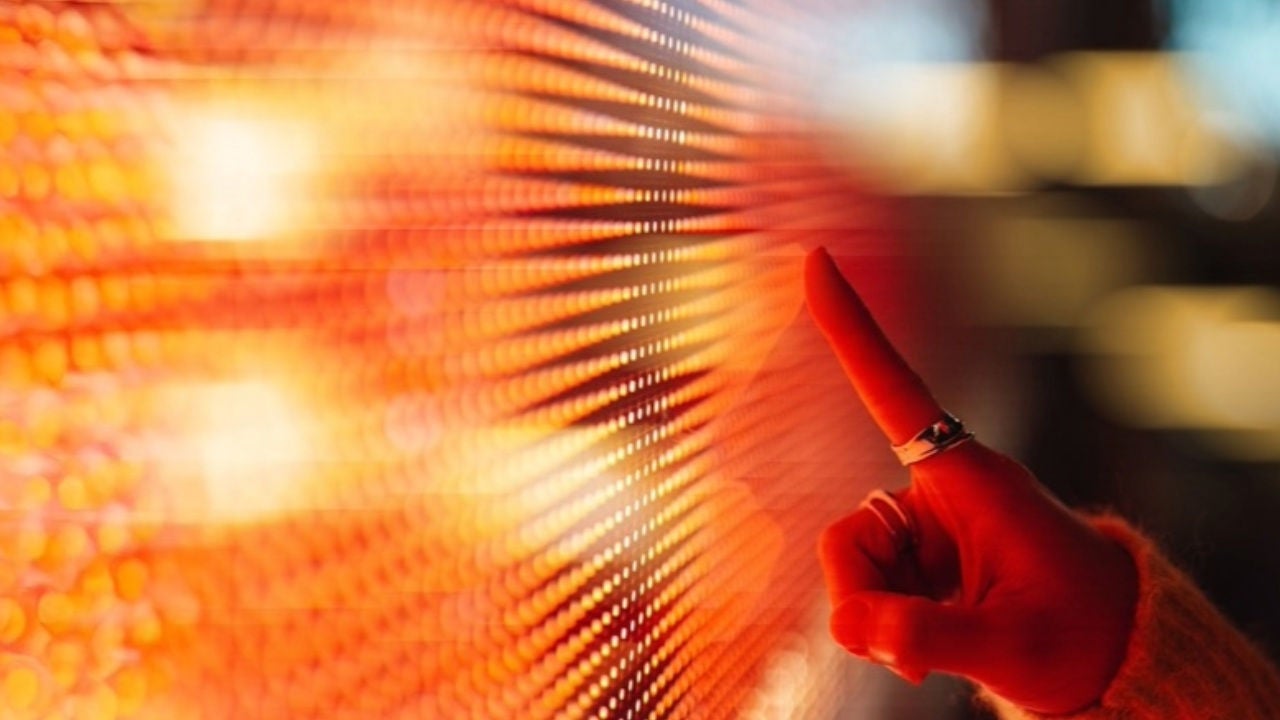 A woman touches a glowing screen with one finger. 