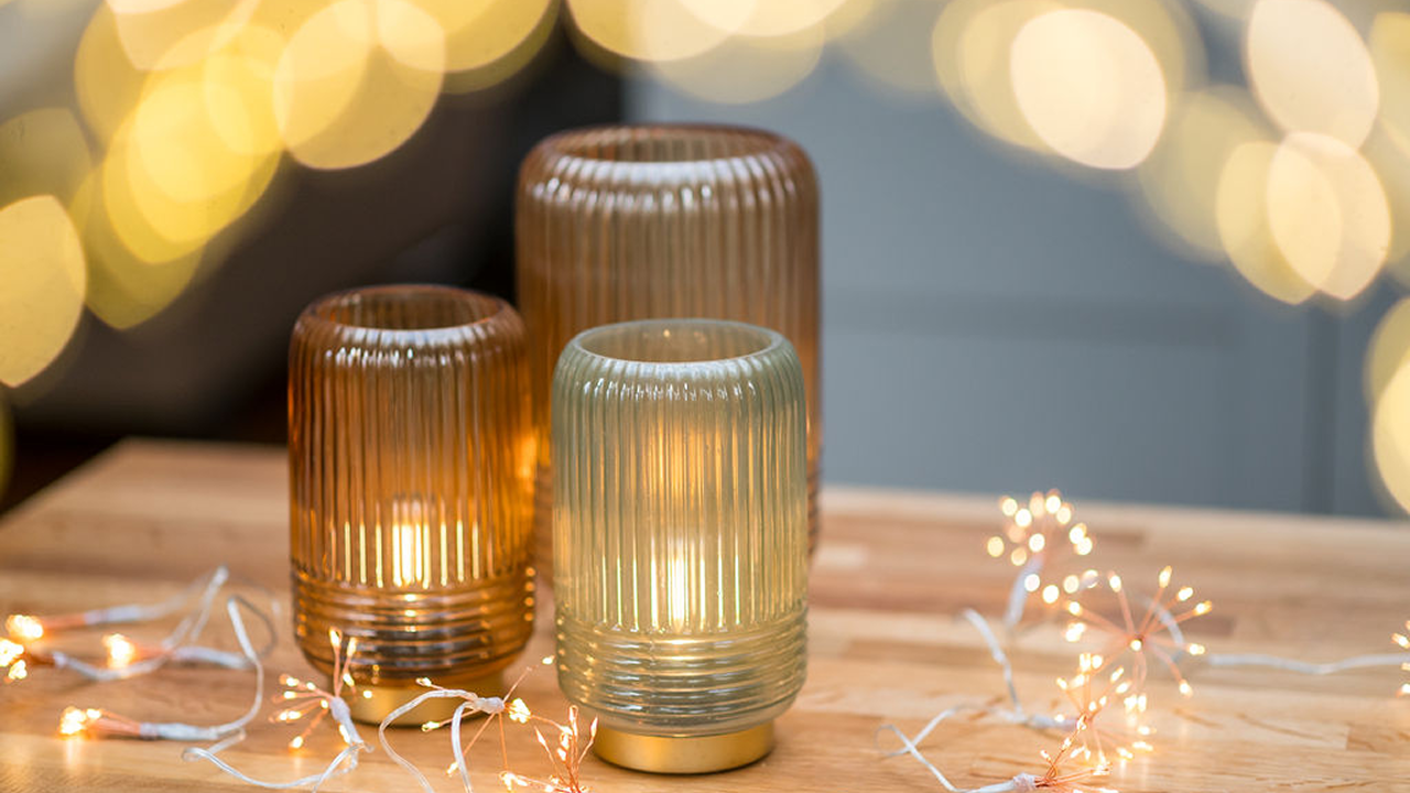 A couple of lit up candles on a table with string lights beside