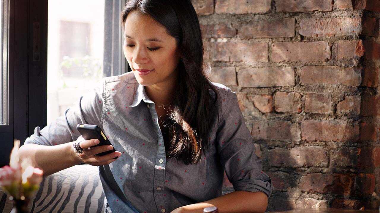 Nő okostelefont használ egy kávézóban.