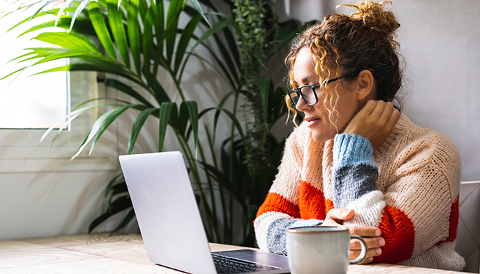 Serene young mature woman looking and reading on laptop online notification email