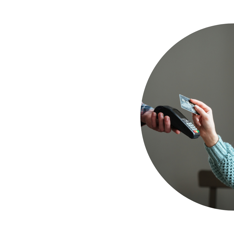 Közeli részlet egy érintésmentes kártyás fizetésről, ahol egy vásárló bankkártyát tart egy terminálhoz, sötét háttér előtt.