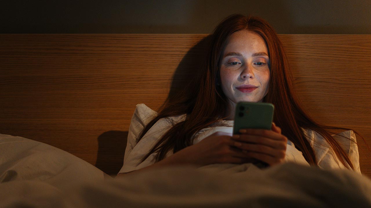 Woman scrolling on phone in bed.