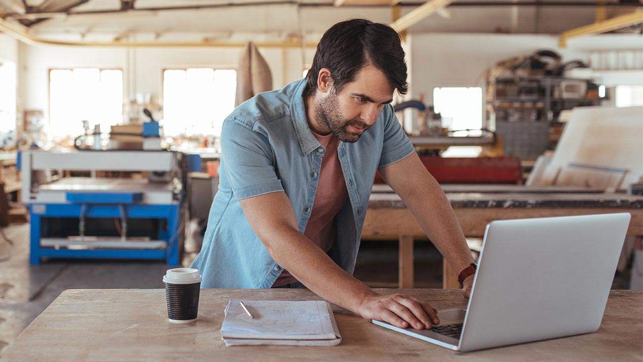 Young woodworker using a laptop in his workshop.