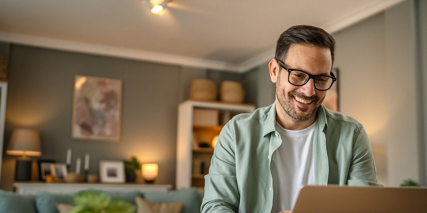 A man in a green shirt smiling while using his computer at home