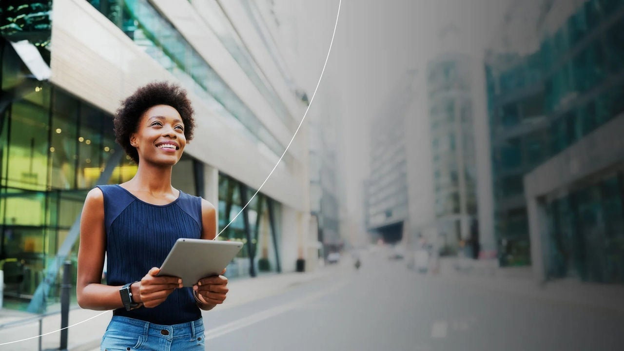 אישה מחזיקה טאבלט מול בנייני משרדים.