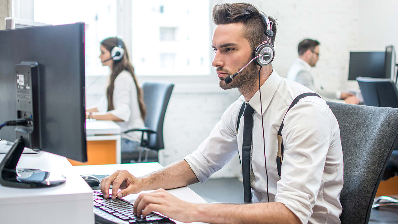 Ügyfélszolgálati munkatárs headsettel ül az irodában, és számítógépen dolgozik.