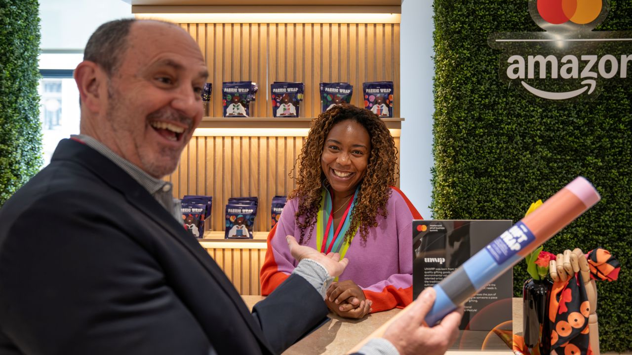 A customer holds fabric gift wrap and points to the small business owners selling fabric wraps at the marketplace at the Mastercard Small Business Summitt in New York City. 