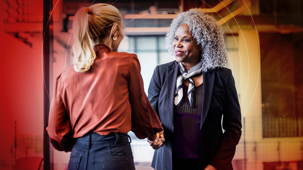 Professional handshake between two businesswomen in a modern office setting.
