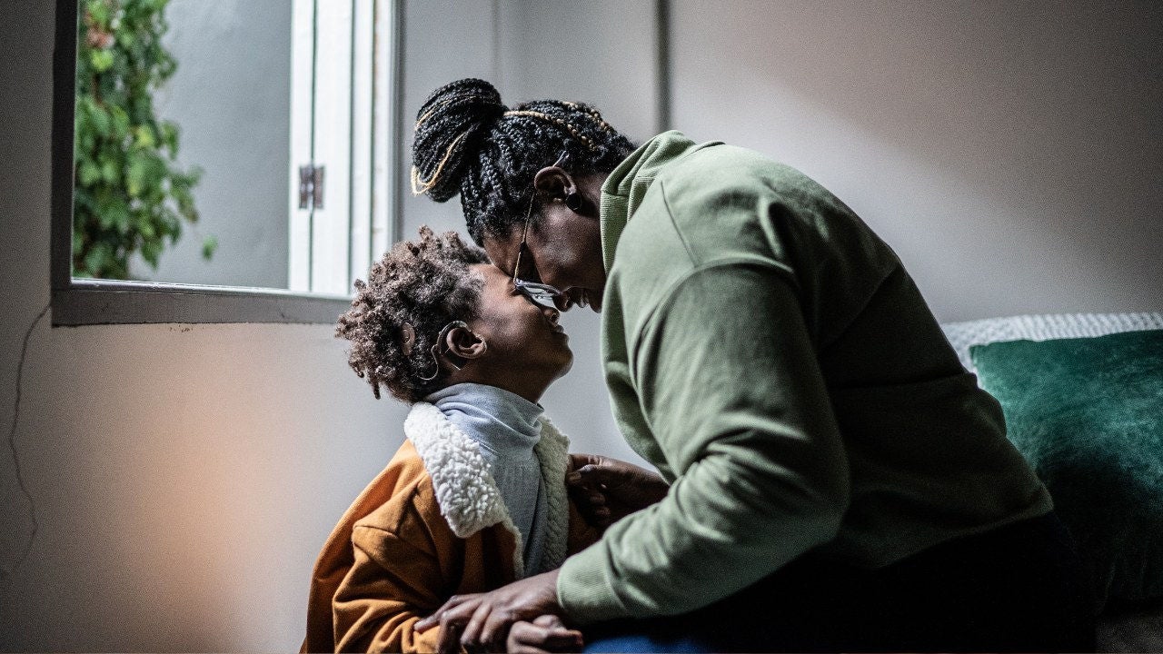A mother and her young son touch foreheads in a living room. 