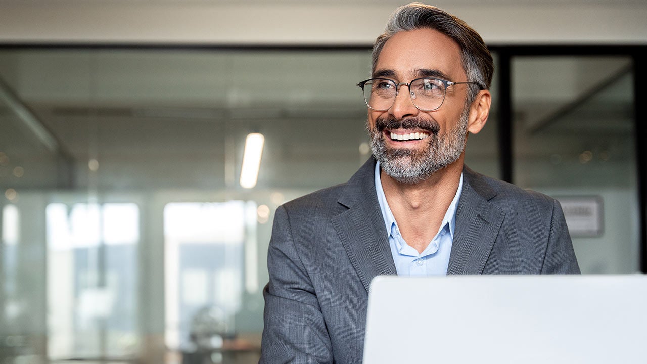 A smiling man using laptop in corporate office.