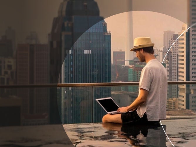 Man sitting on ledge of infinity pool at the top of a building looking at his laptop