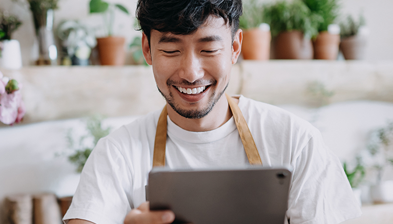 Man surrounded by flowers smiling at tablet
