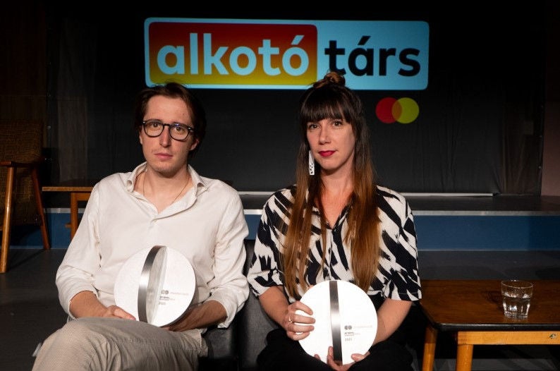 A képen két alkotó ül egy színpadon, kezükben díjjal, mögöttük az „alkotó társ” felirat és a Mastercard logó, ami egy kreatív együttműködéshez kapcsolódó elismerést sugall.