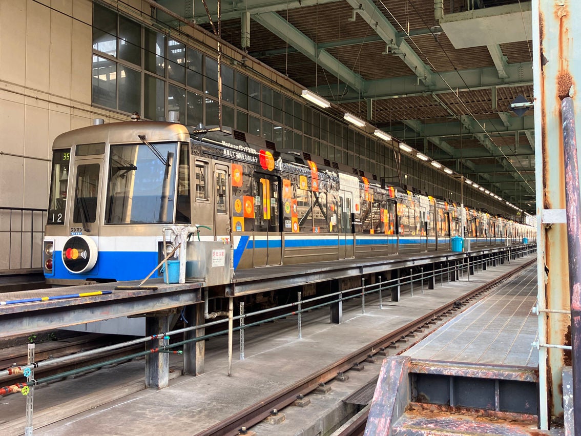 A subway train with a colourful wrapped livery stands at a platform inside a depot.