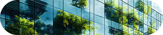 A modern building with large windows reflecting surrounding trees in a clear blue sky.