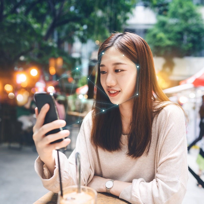 A woman sitting outside looks at her camera for authentication.