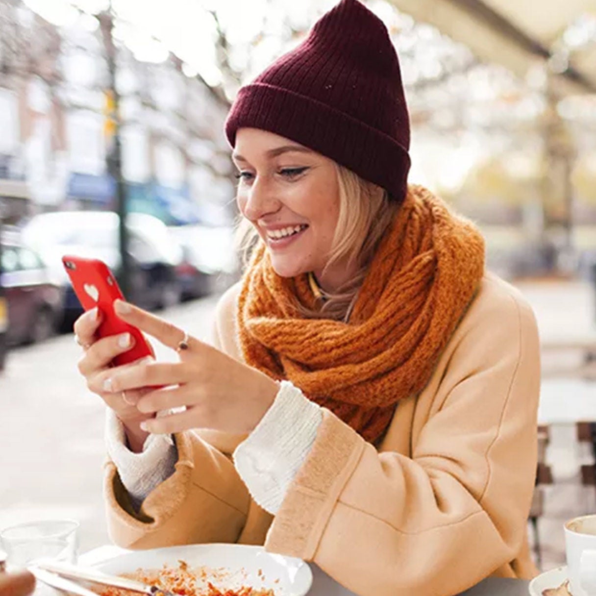 Woman smiling while using her phone outdoors.