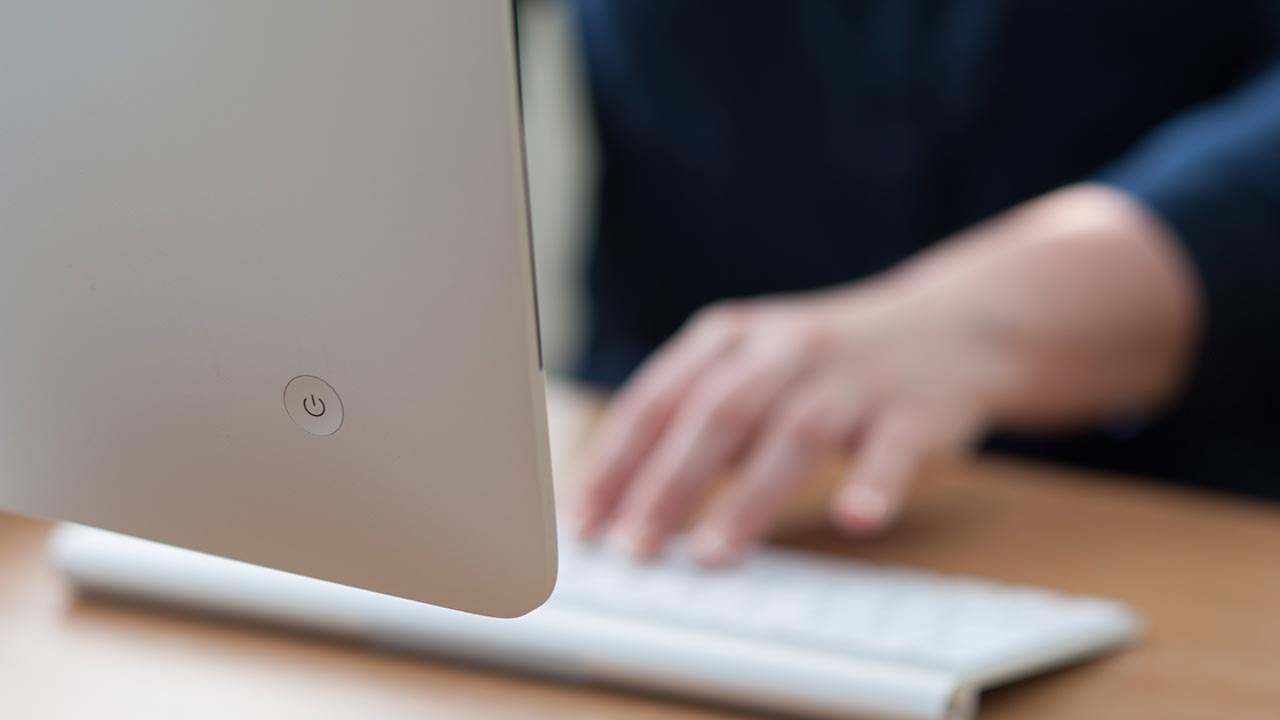 iMAC computer from behind with a hand touching keyboard.