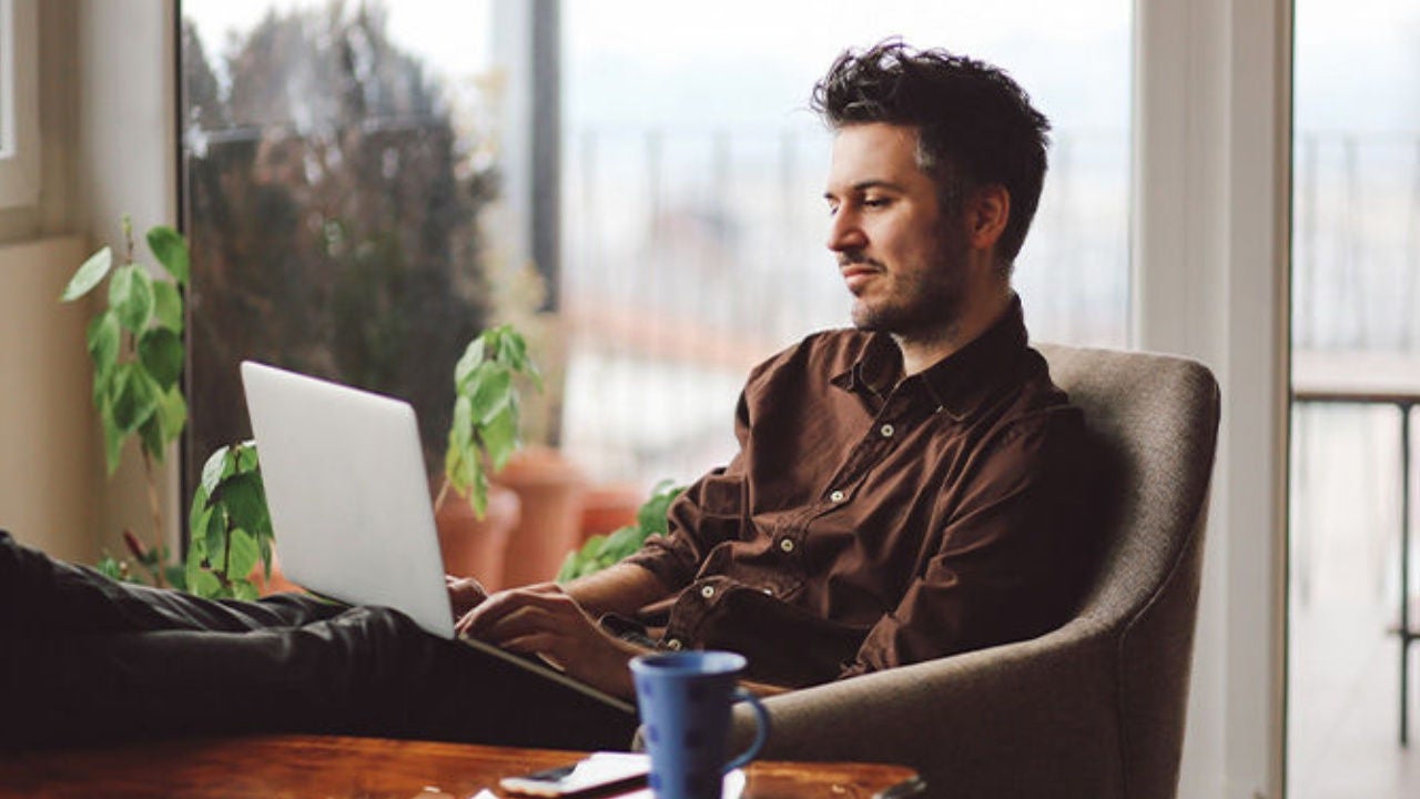A man sits in a chair and looks at his laptop. 