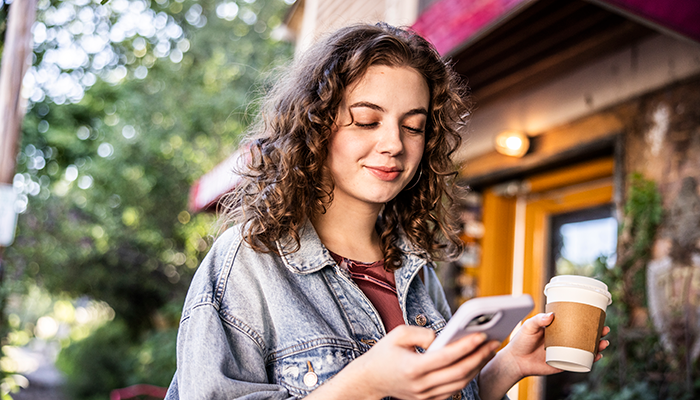 Woman on her phone outside with a coffee in hand