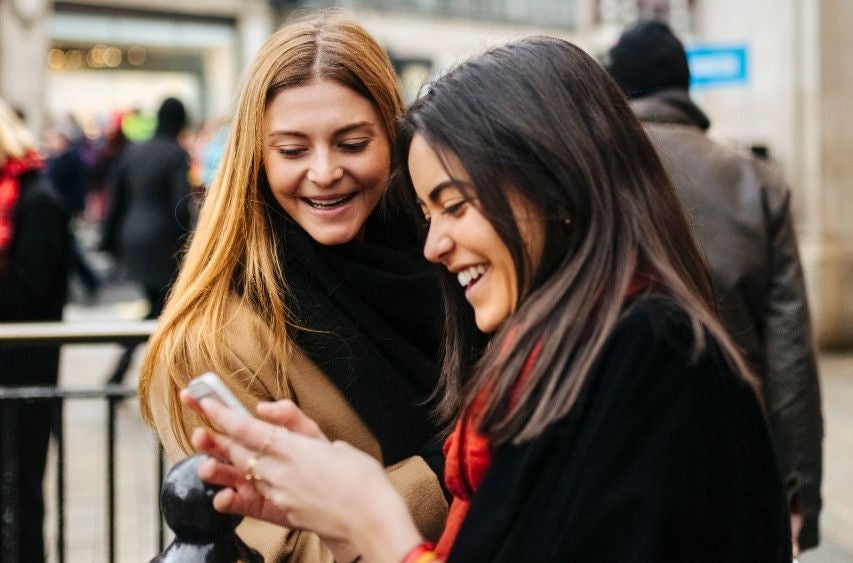 Two young women laughing and looking at a mobile device.