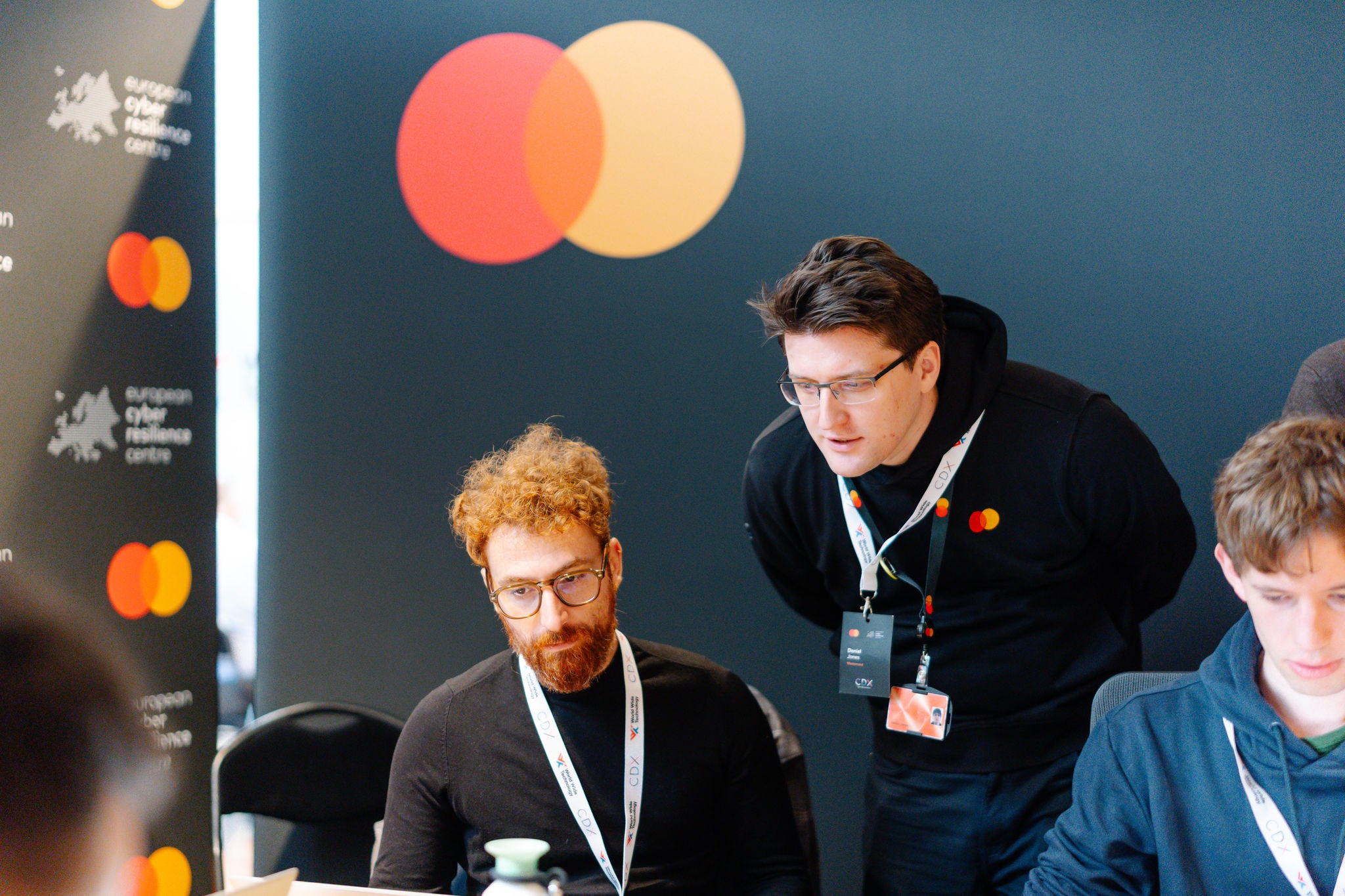 Two men exchange documents on stage during the Mastercard and ENISA memorandum signing.