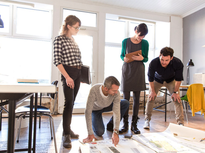 A diverse team of colleagues collaborates over large plans in a modern office, showing small business growth and innovation.