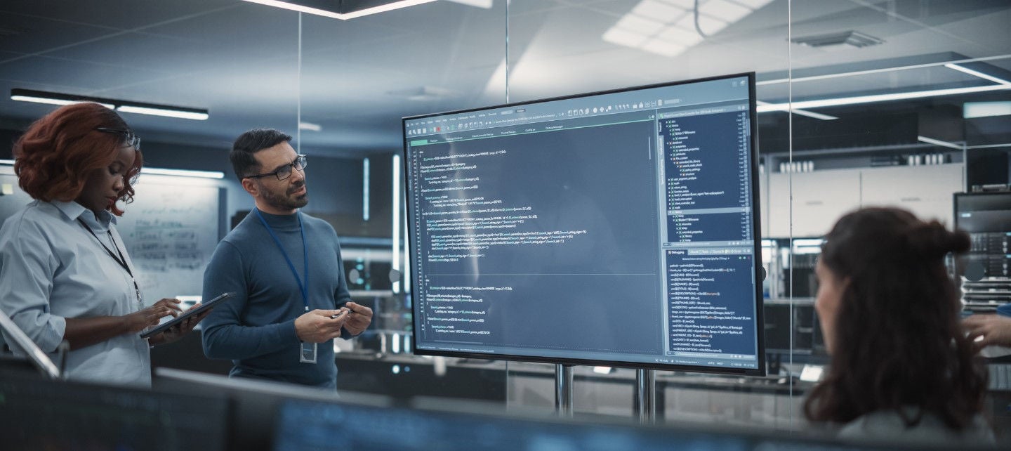 Colleagues look at a large screen with coding on it in an office. 